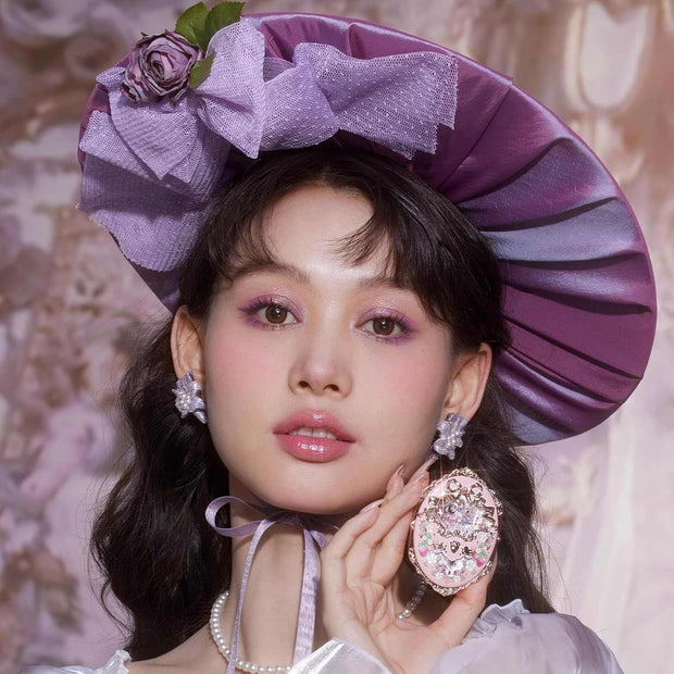 Woman wearing pastel purple hat and makeup showing Strawberry Rococo Embossed Blush compact with rosy cheeks and smooth, radiant finish