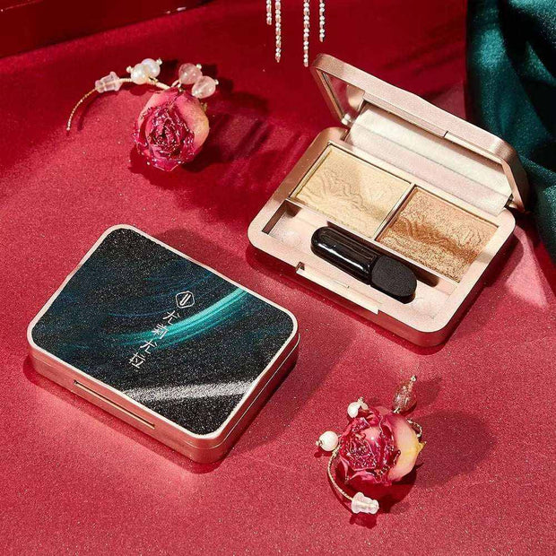 Compact makeup set gift box with eyeshadow palette and applicator on red satin background