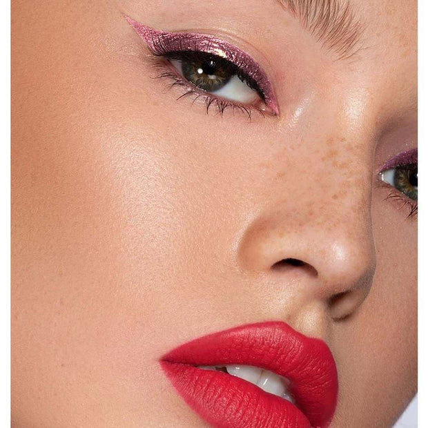 Close-up of eye with shimmering pink glitter liquid eyeliner and bold red lipstick on smooth skin